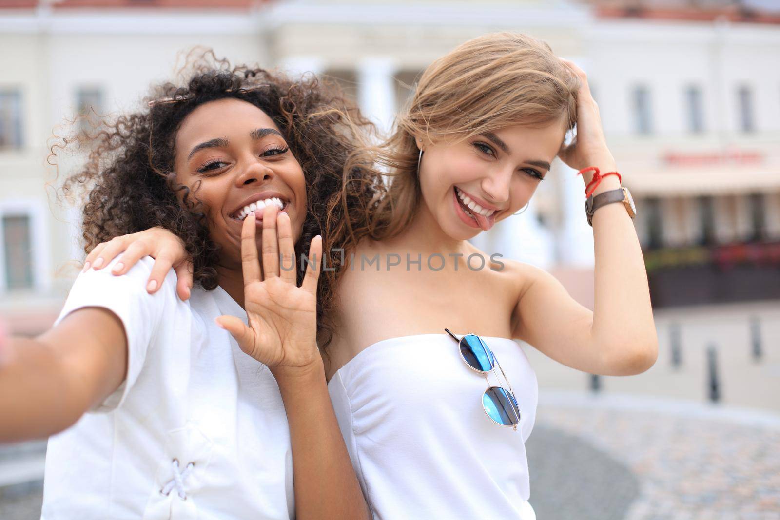 Young smiling hipster women in summer clothes posing on street.Female showing positive face emotions