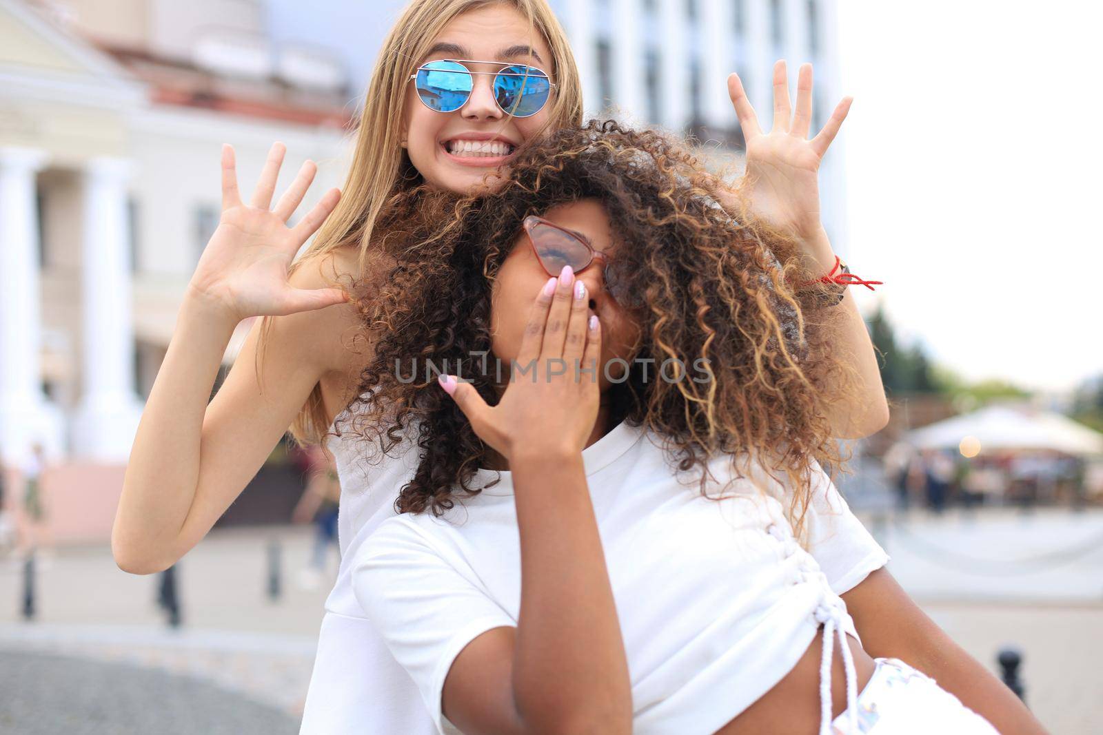 Young smiling hipster women in summer clothes posing on street.Female showing positive face emotions