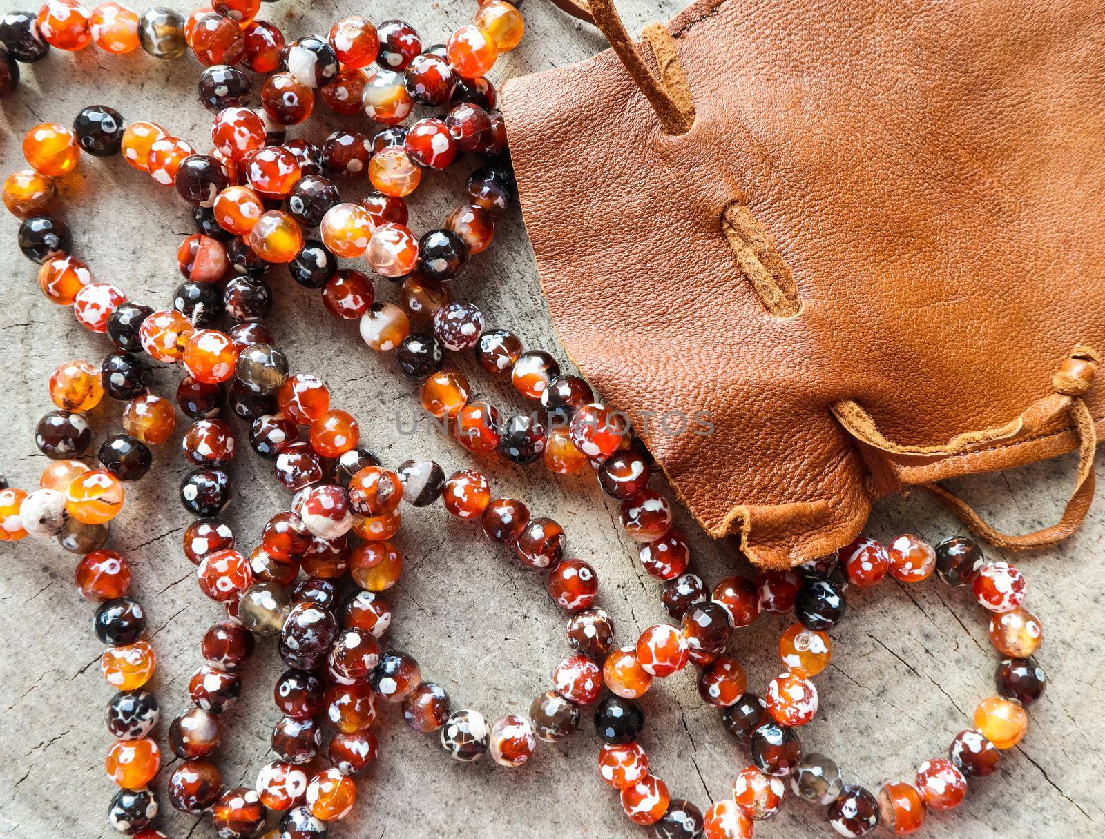 Sunny beads of amber fireplace faceted agate with leather jewelry pouch bag on rustic background by Olayola