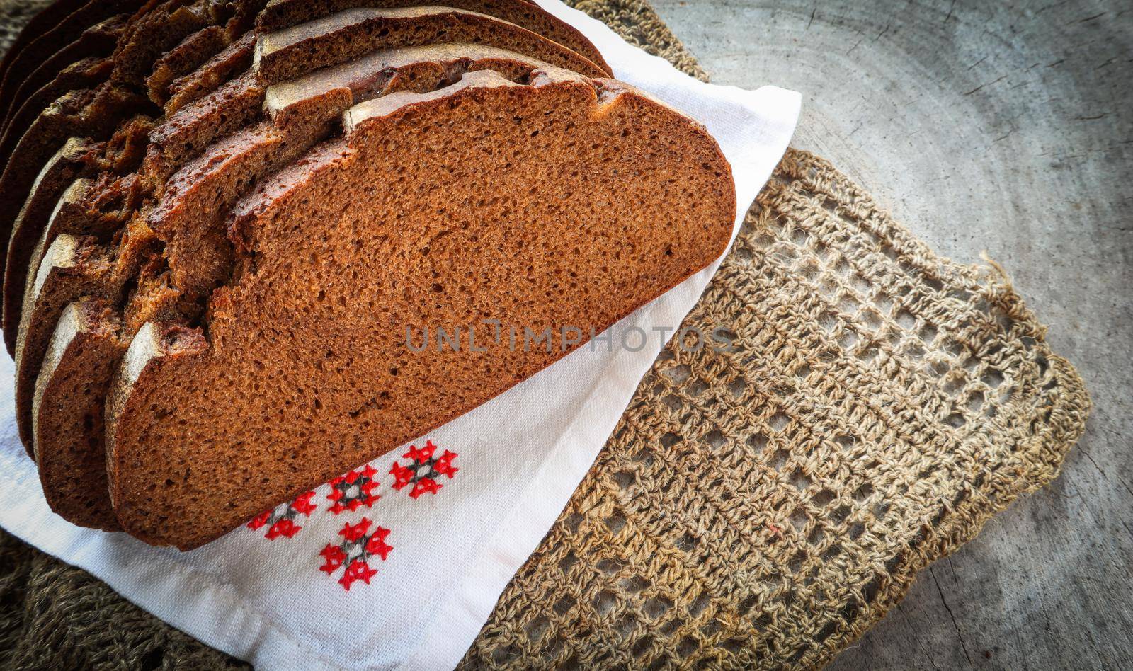 Fresh rye sliced bread, natural linen napkin and white serviette with cross-stitch on rustic wooden background