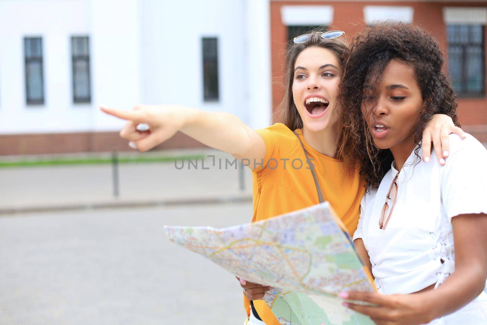 Holidays and tourism concept - beautiful girls looking for direction in the city