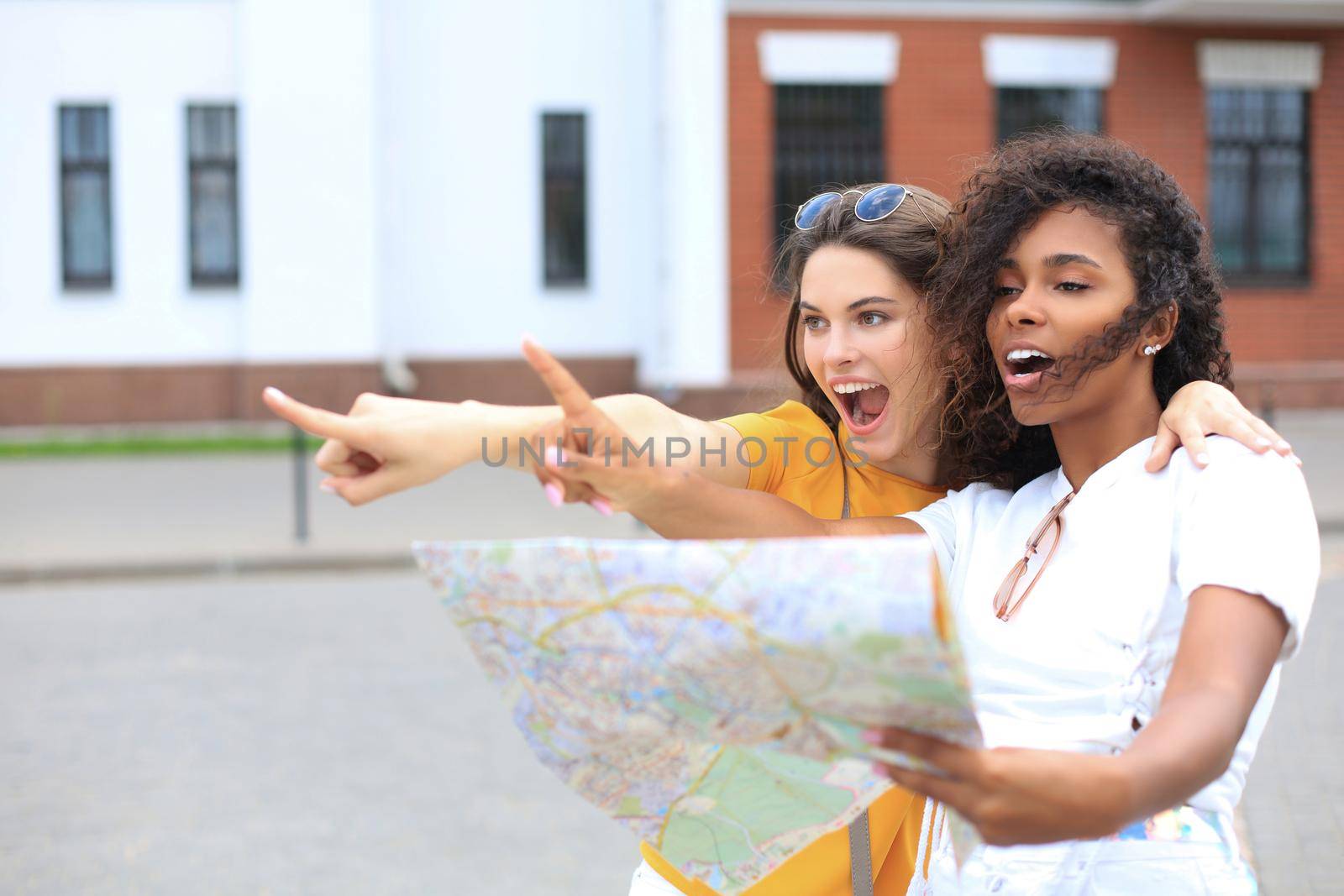 Holidays and tourism concept - beautiful girls looking for direction in the city