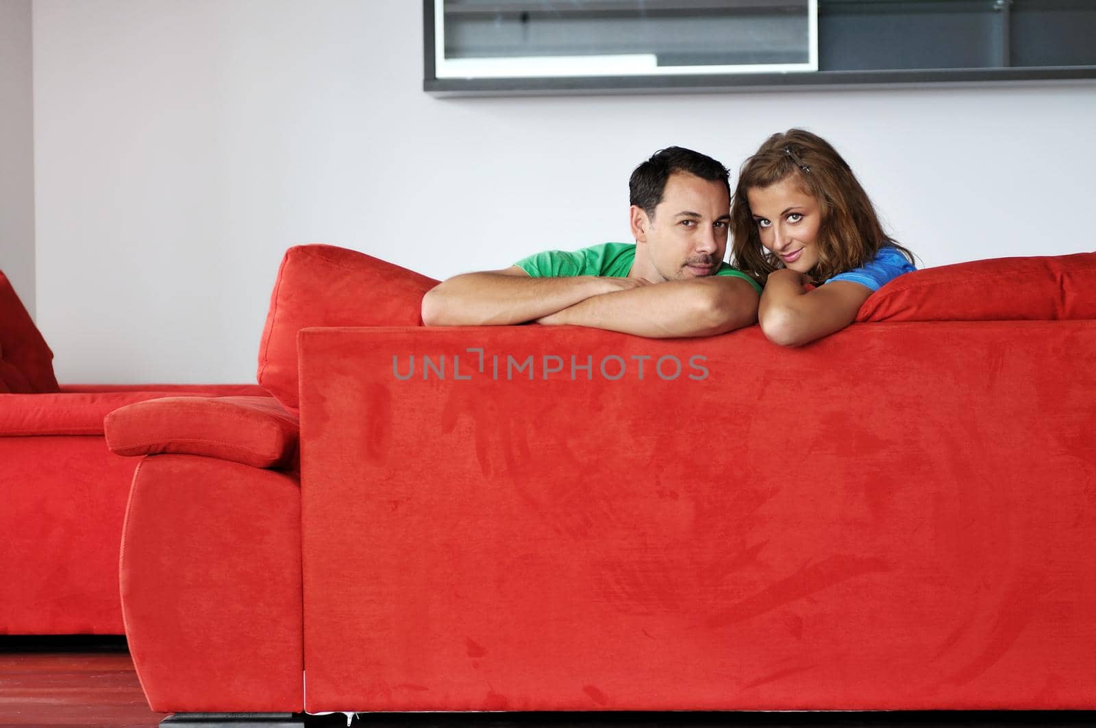 happy couple relaxing on red sofa in big bright new apartment