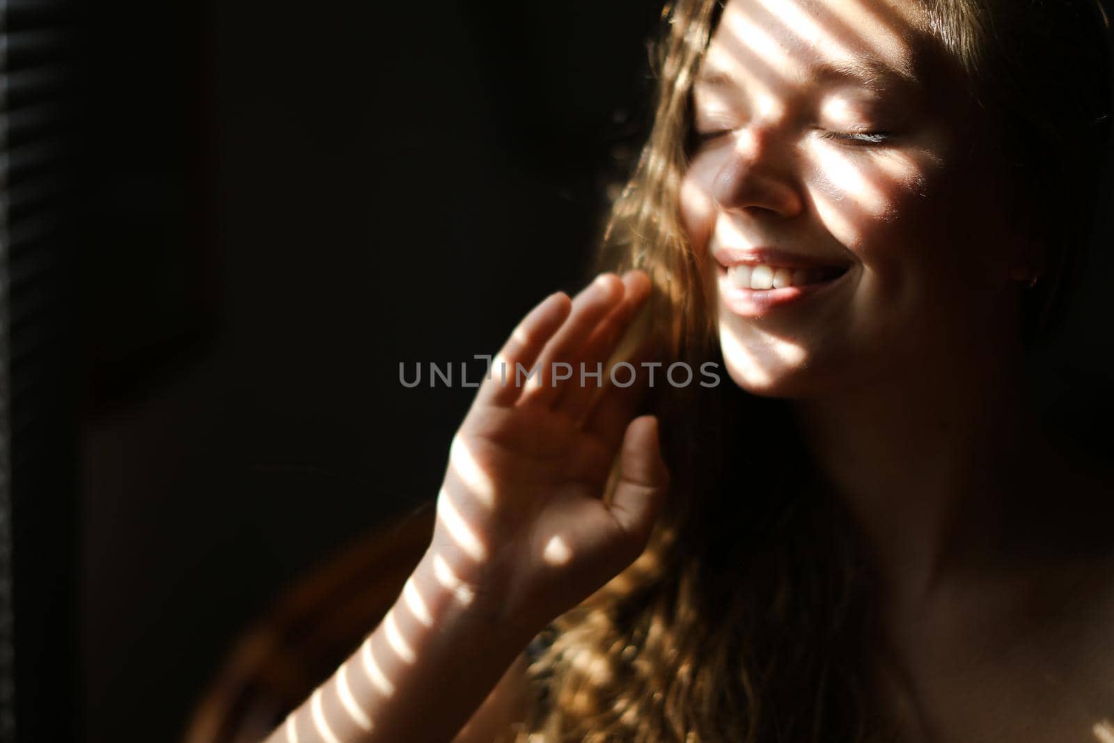 Close up portrait of young smiling girl with closed eyes and striped shadows. Concept of private photo session and beautiful femaleperson with eveday makeup.