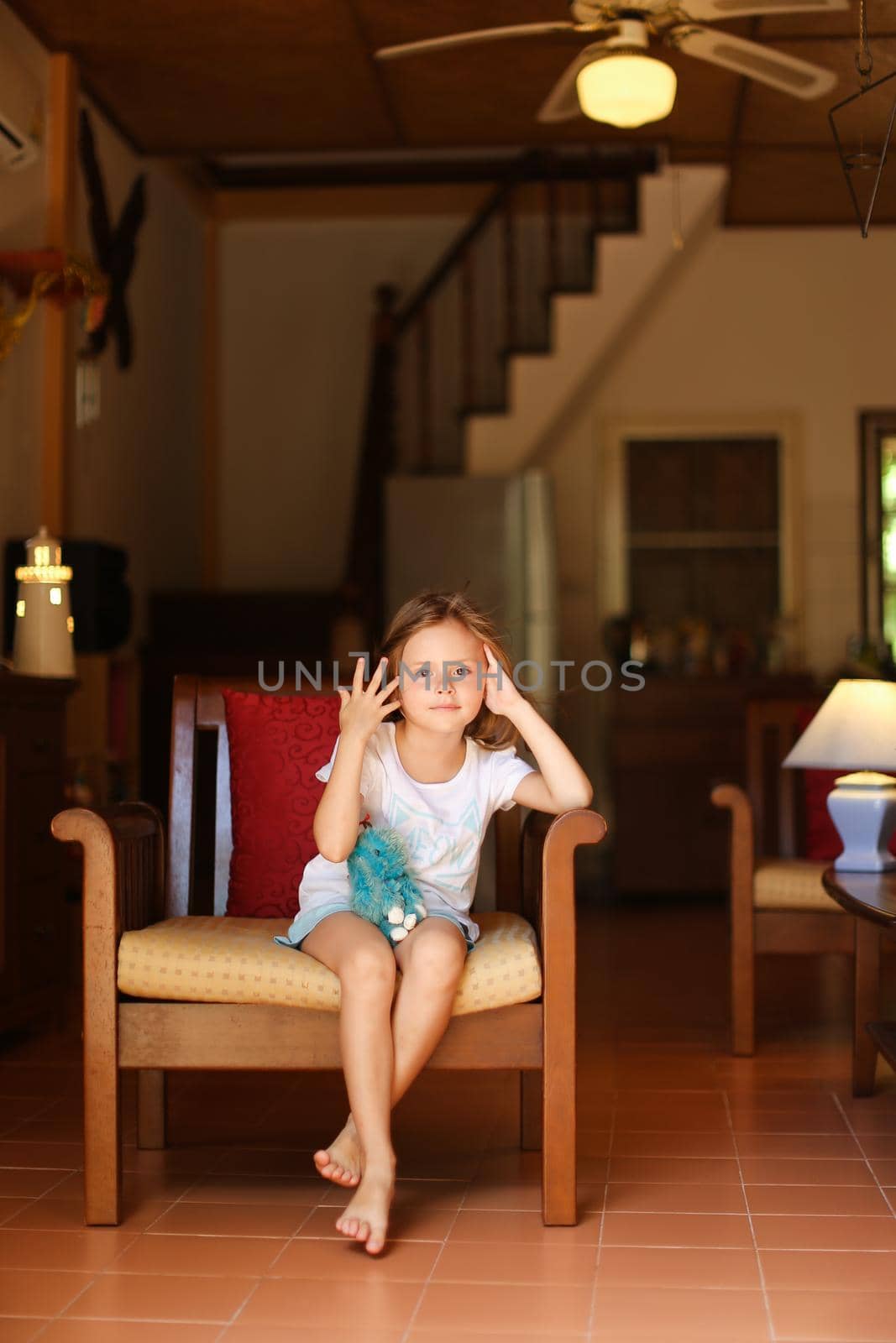 Little female kid sitting in chair with in living room. Concept of leisure time for children and wooden interior.