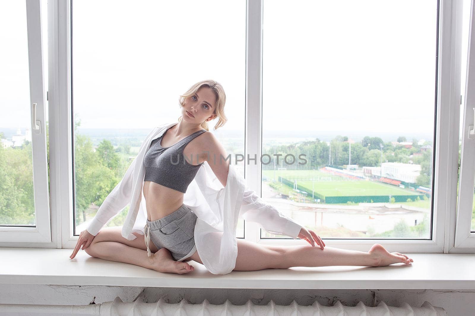 girl practicing yoga, doing splits, stretching exercise on windowsill at home by artemzatsepilin