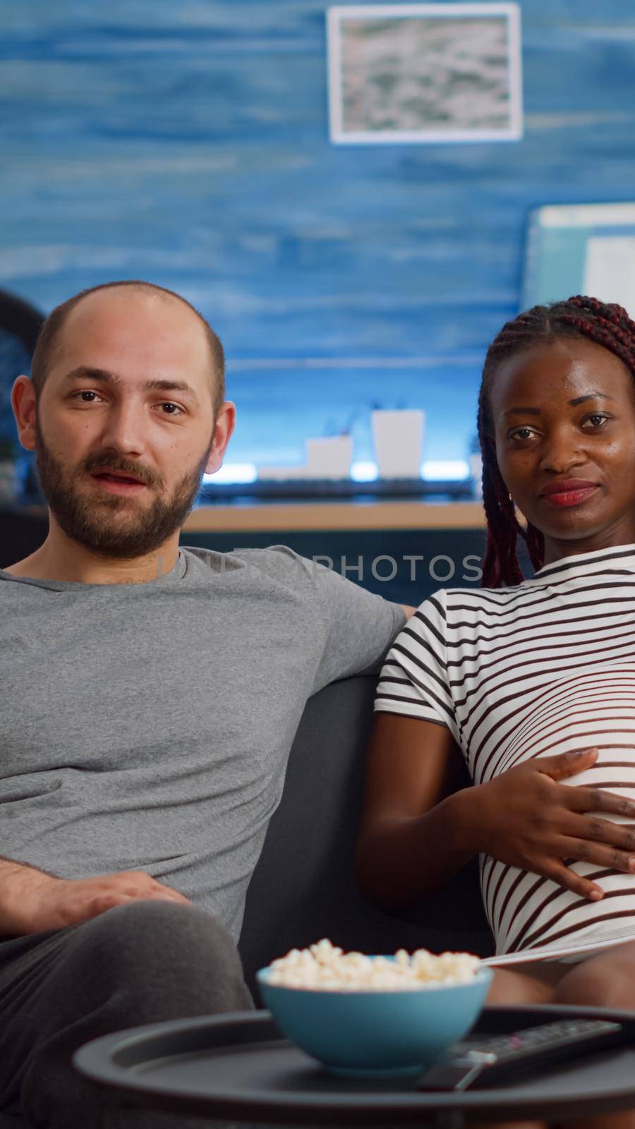 Pregnant interracial couple using video call conference for remote online communication at home. Mixed race people expecting baby, talking to friends with technology in living room