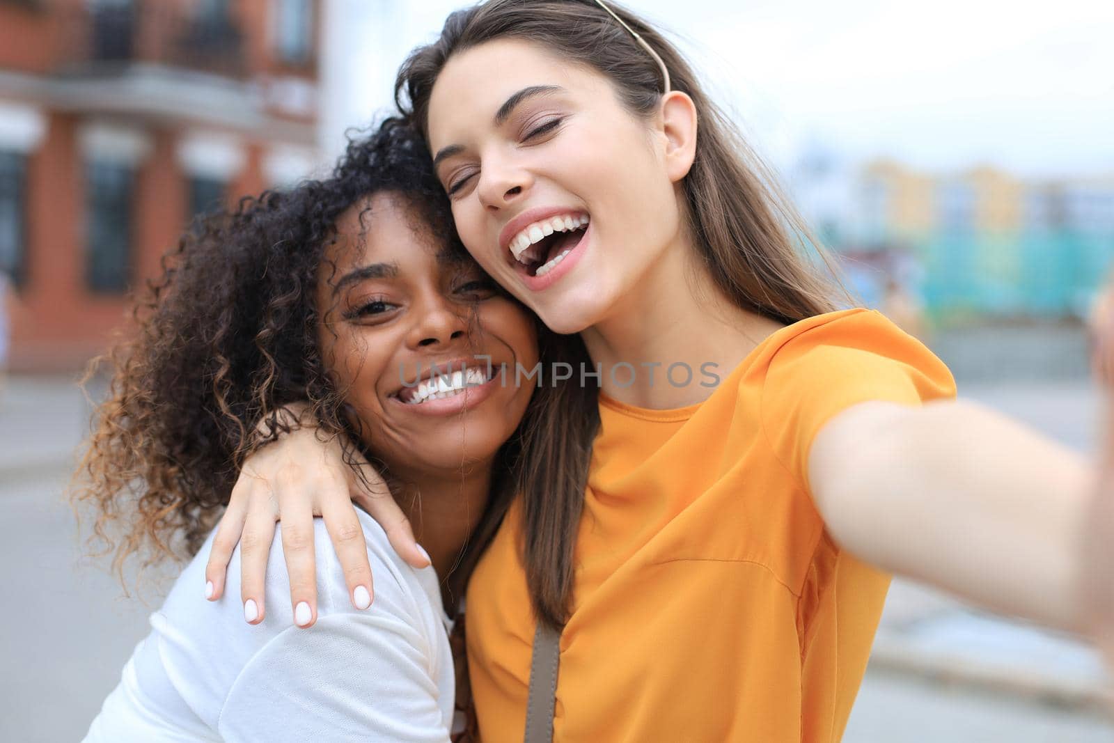 Two laughing friends enjoying weekend together and making selfie on city background