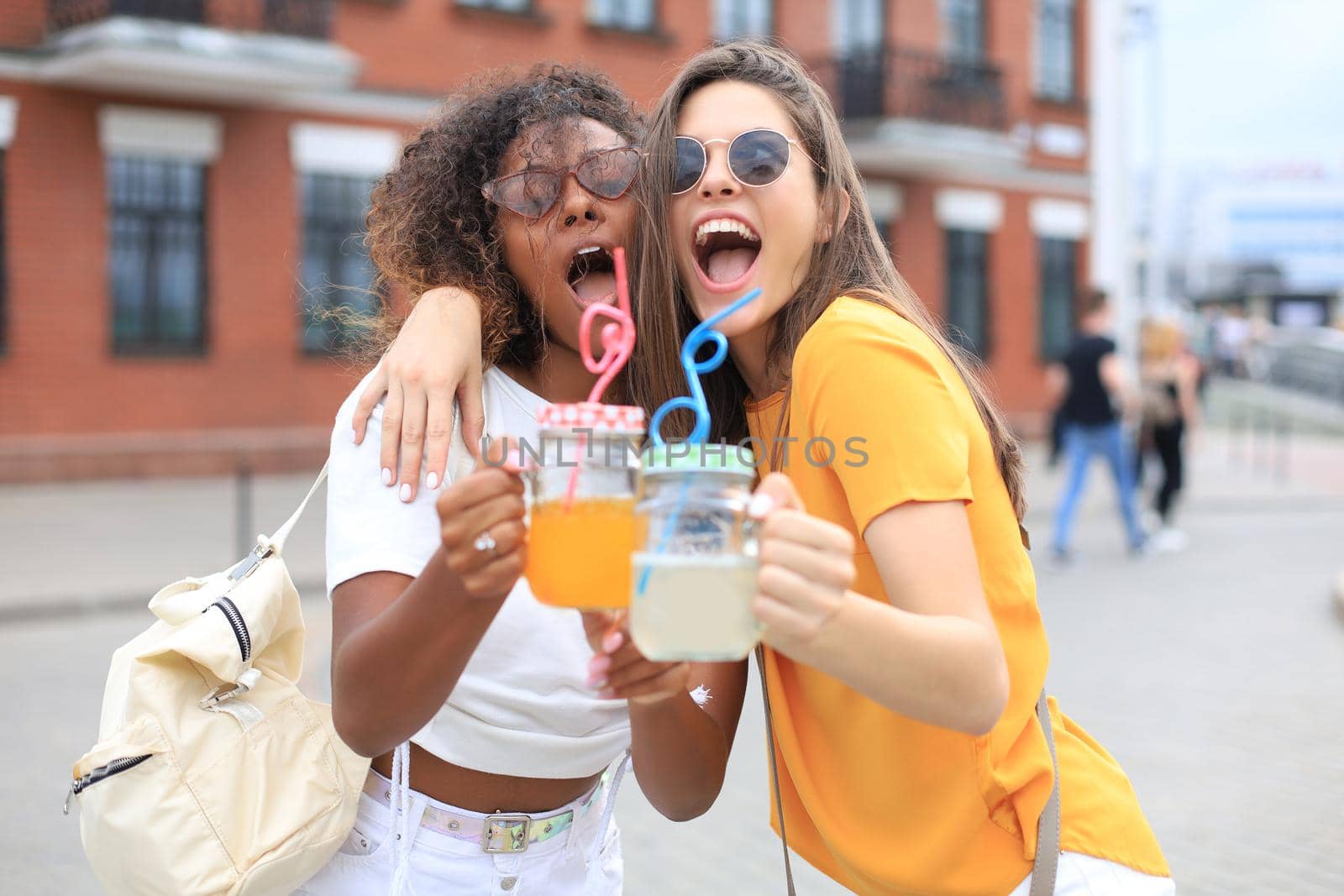 Trendy cool hipster girls, friends drink cocktail in urban city background