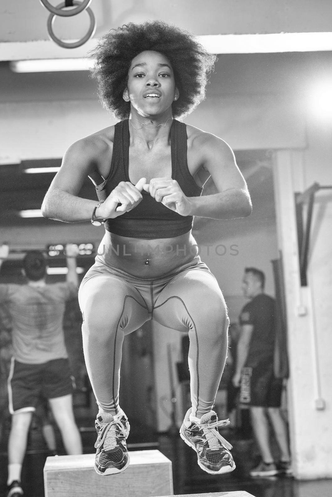 Fit young african american woman box jumping at a crossfit style gym. Female athlete is performing box jumps at gym.