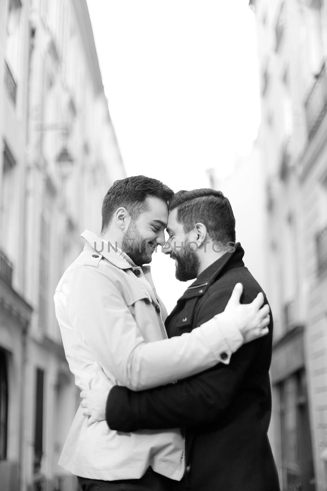 Black and white photo of two hugging gays in city, buildings i background. Concept of same sex couple nad love.