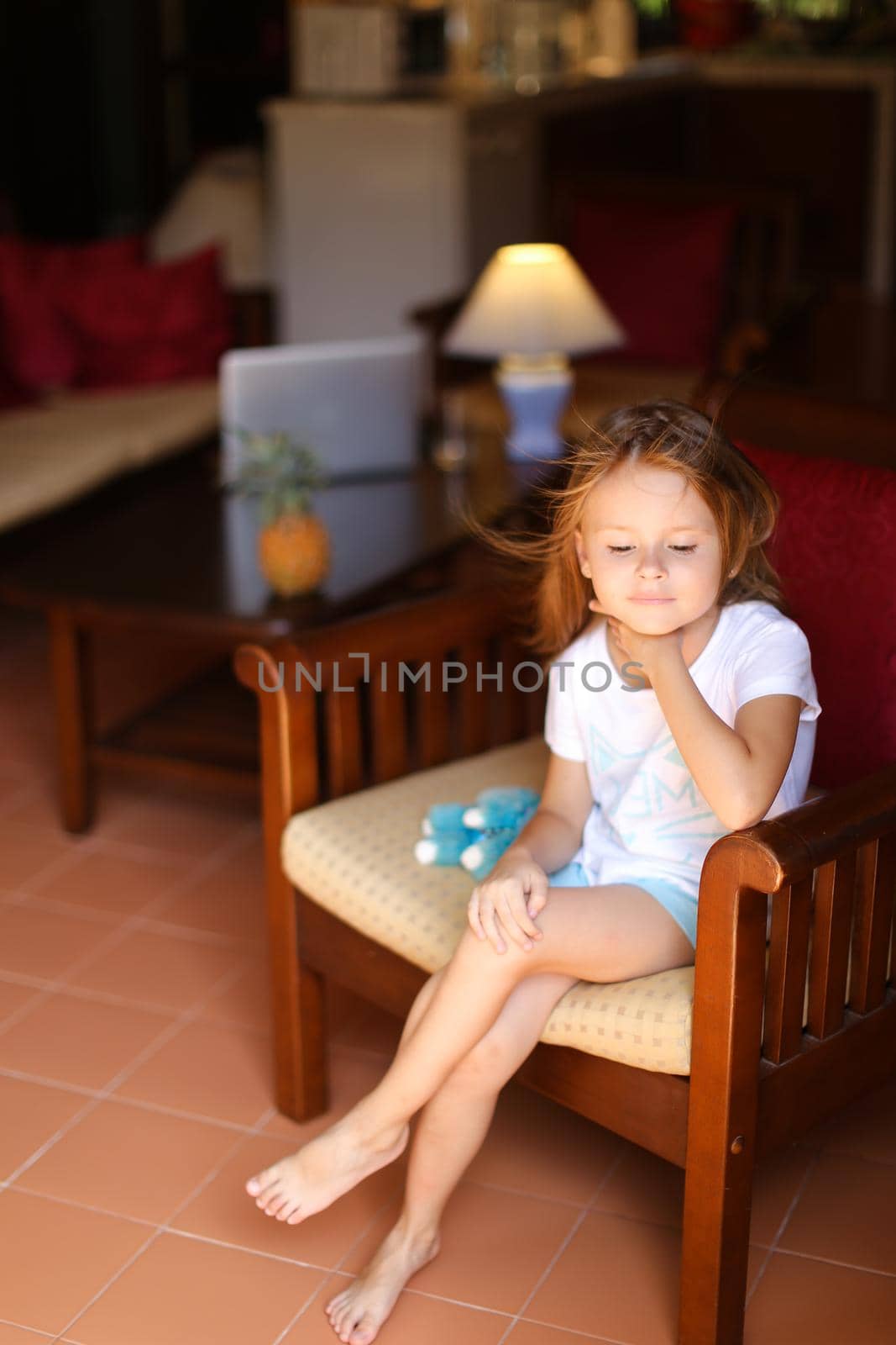 Little european female kid sitting with toy in wooden chair. Concept of kid model and wood in interior.