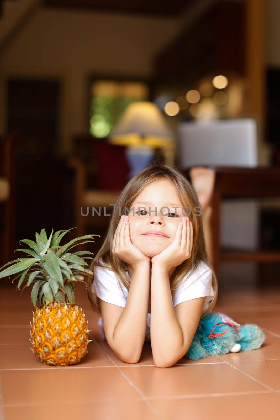 Portrait of little barefoot girl lying on floor with pineapple and toy. by sisterspro