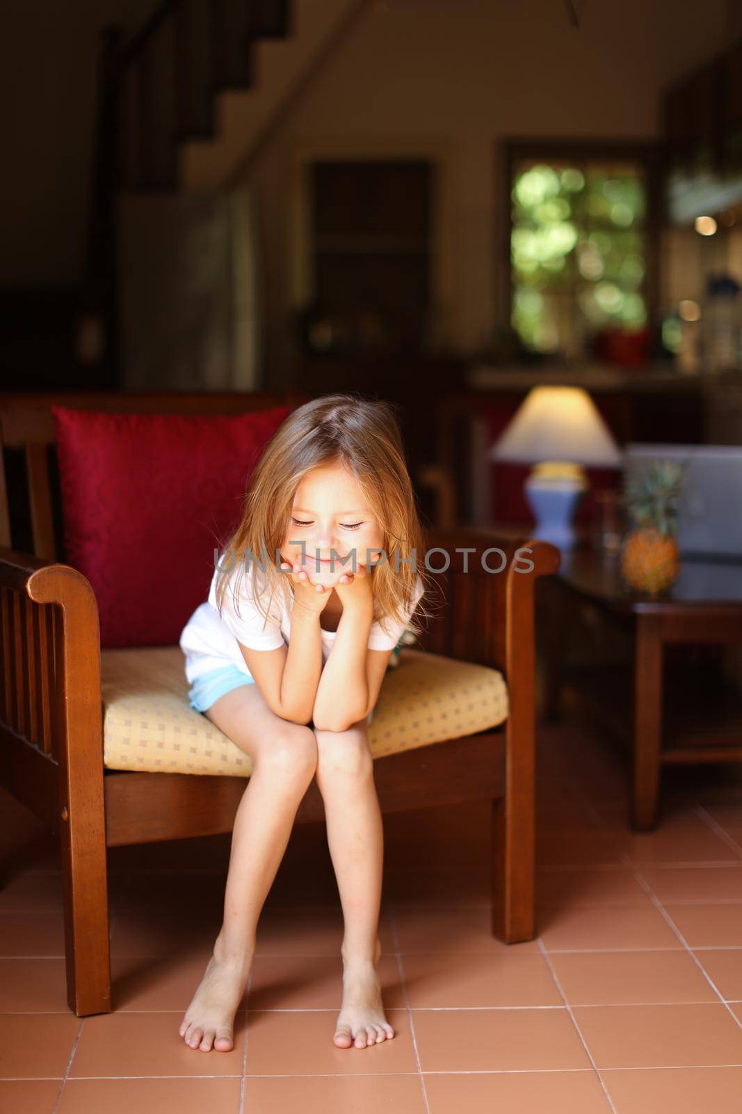 Female caucasian kid sitting in wooden chair in living room. Concept of child model and cozy interior.