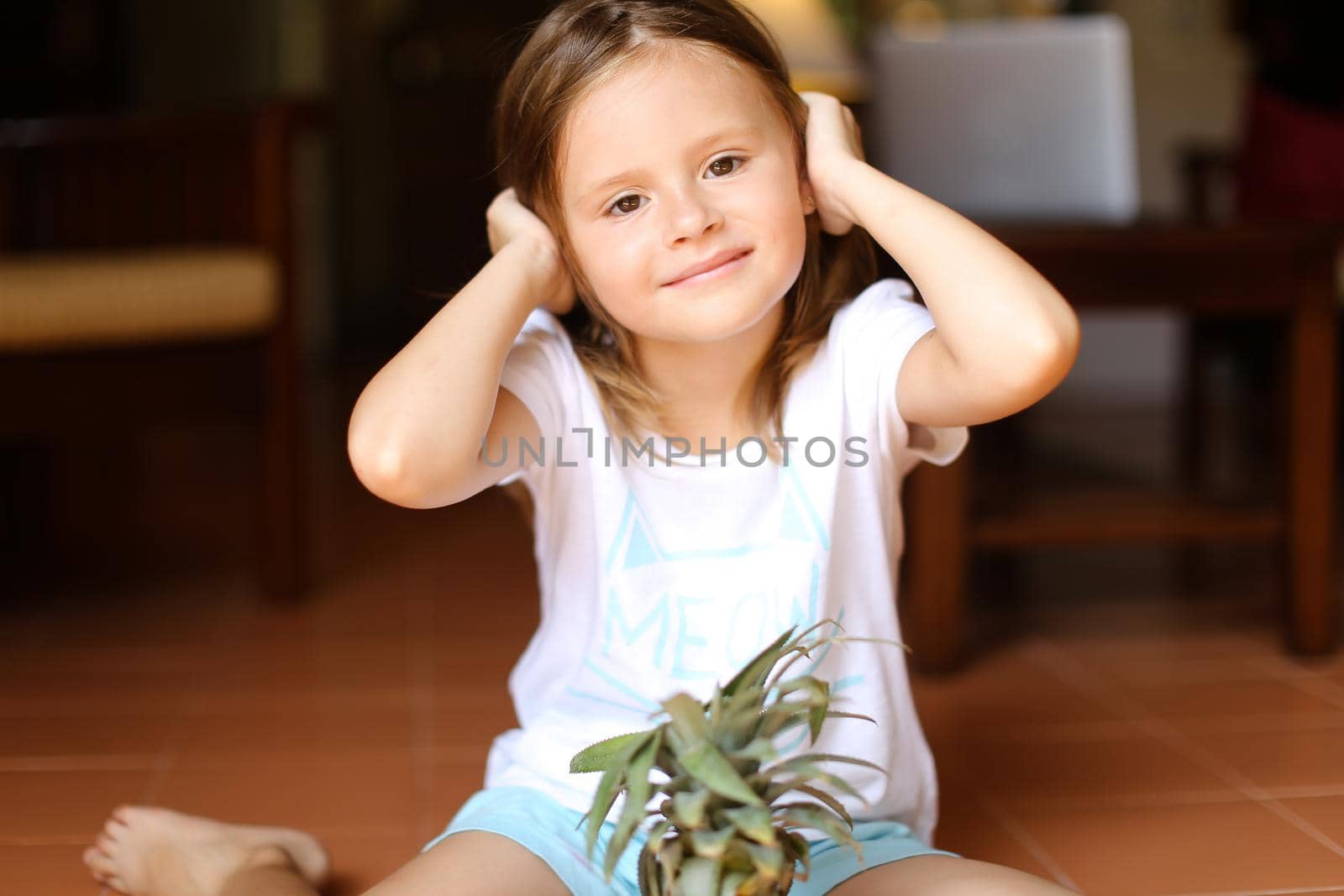 Portrait of little female barefoot kid sitting on floor with pineapple. Concept of fruits and children.