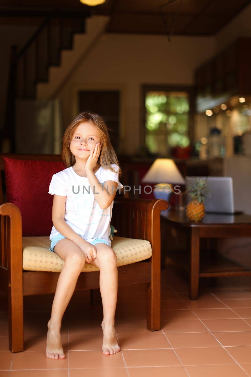 Little happy girl sitting in wooden chair in living room. by sisterspro