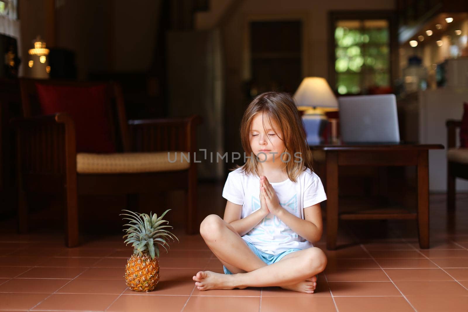 Little girl sitting on floor with pineapple and meditating. by sisterspro