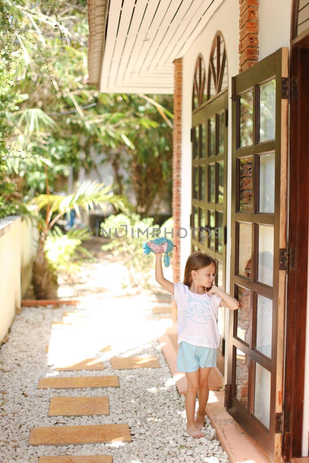 Little barefoot girl standing near door and playing with toy outside. by sisterspro