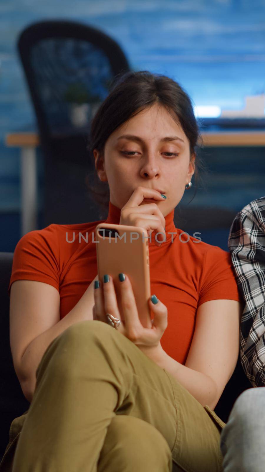 Married interracial couple using smartphone at home. Multi ethnic partners talking while looking at modern device and sitting on couch in living room. Mixed race people with technology