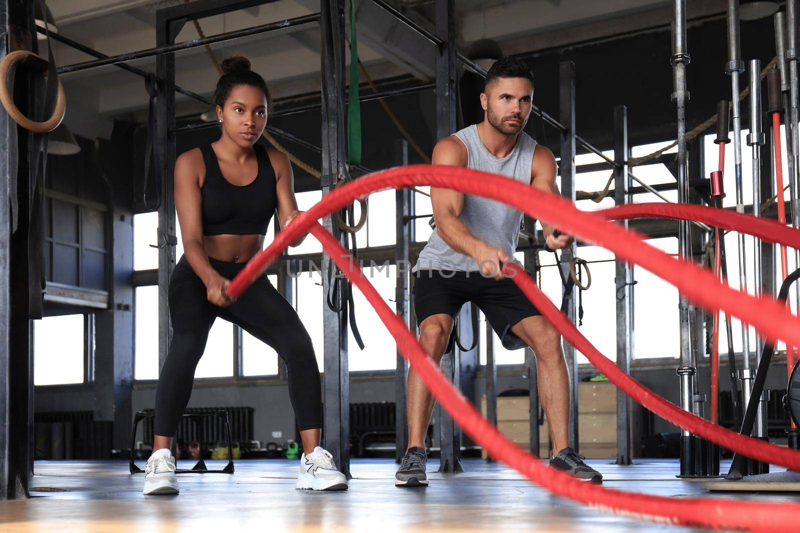 Athletic young couple with battle rope doing exercise in functional training fitness gym