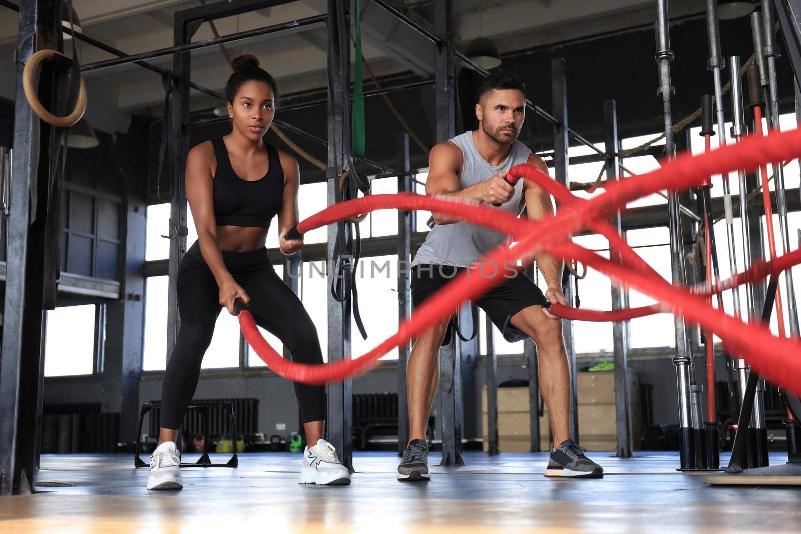 Athletic young couple with battle rope doing exercise in functional training fitness gym