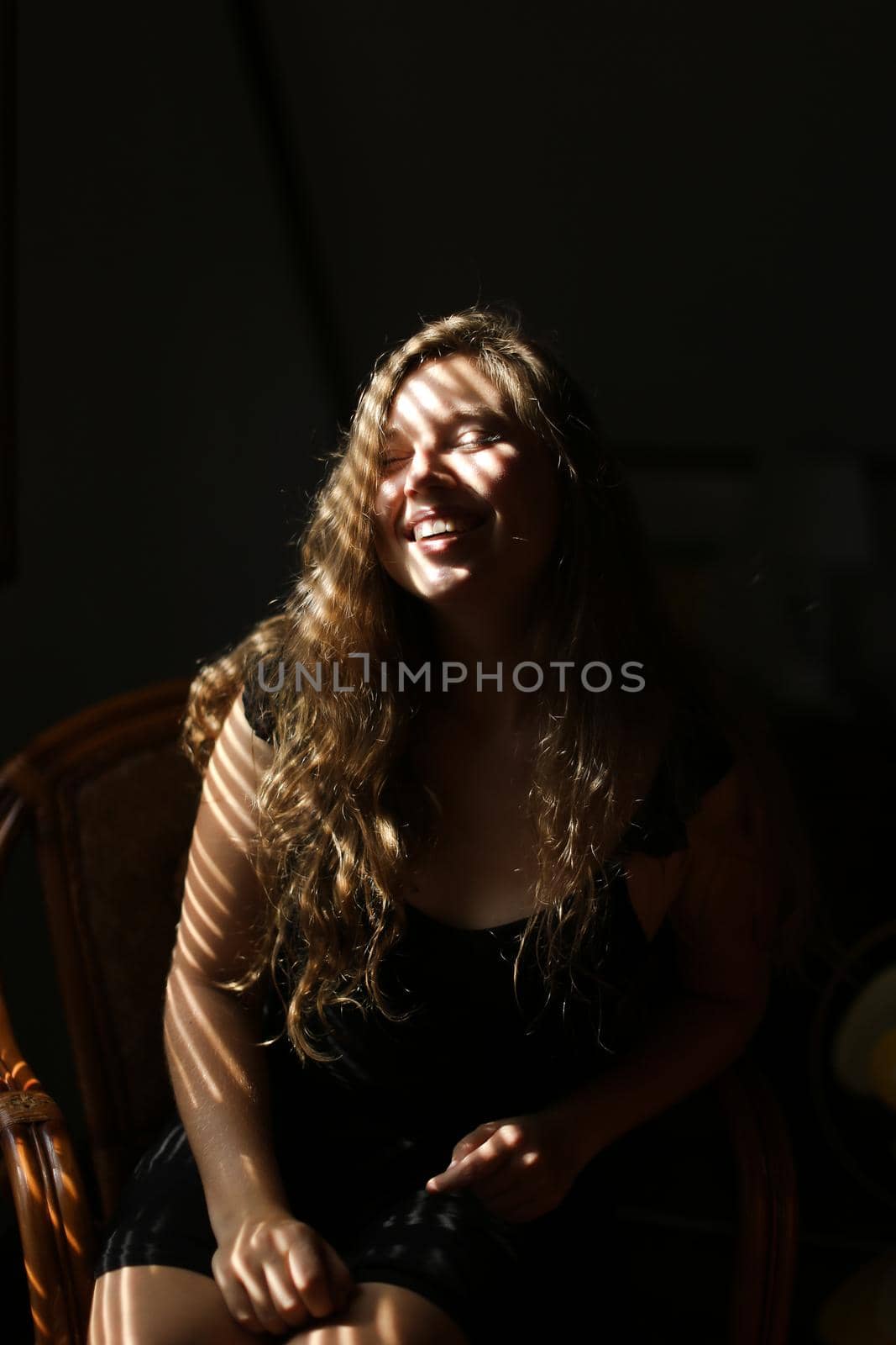 Portrait of young beautiful woman sitting in chair, striped shadows. Concept of female beauty and home photo session.
