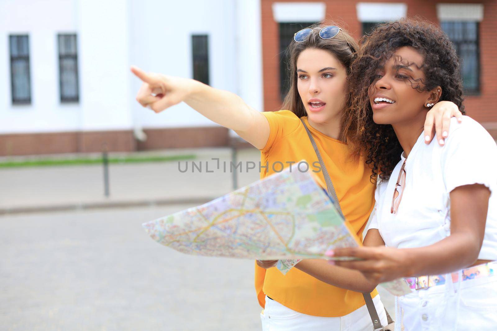 Photo of two girls enjoying sightseeing outdoor. Beautiful female tourists exploring city with map