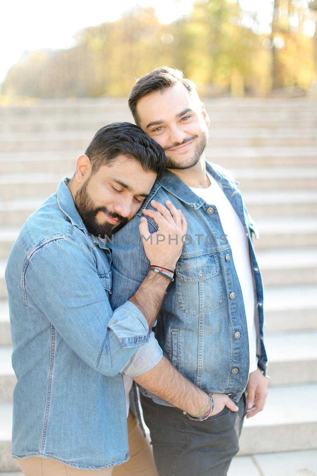 Caucasian young gays hugging in concrete stairs background and wearing jeans shirts. Concept of same sex couple and relationship.
