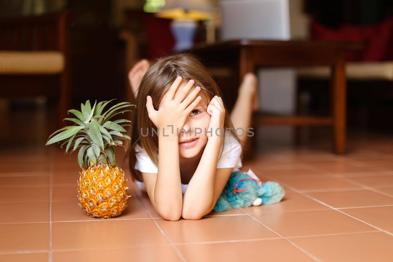 Portrait of little nice girl lying on floor with pineapple and toy. by sisterspro