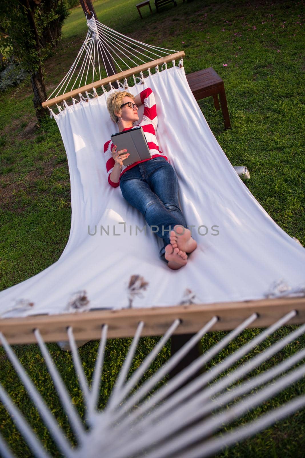 woman using a tablet computer while relaxing on hammock by dotshock