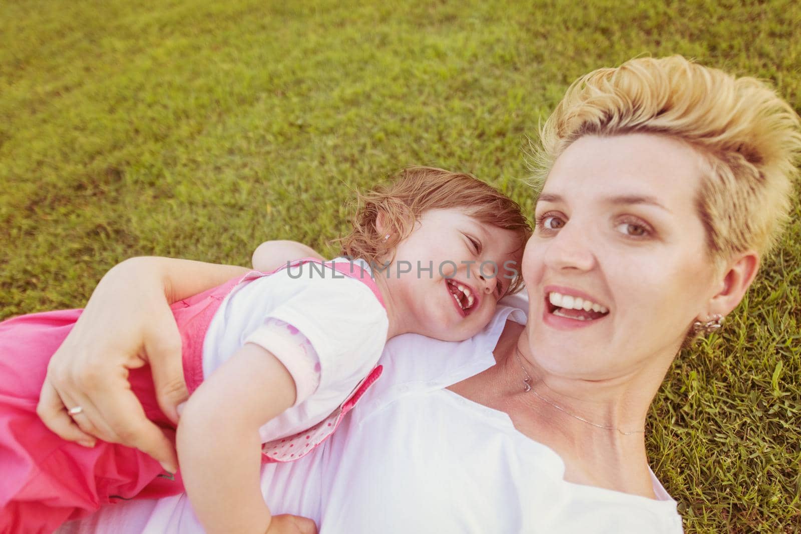 Young Mother and cute little daughter enjoying free time playing outside at backyard on the grass, happy family in nature concept