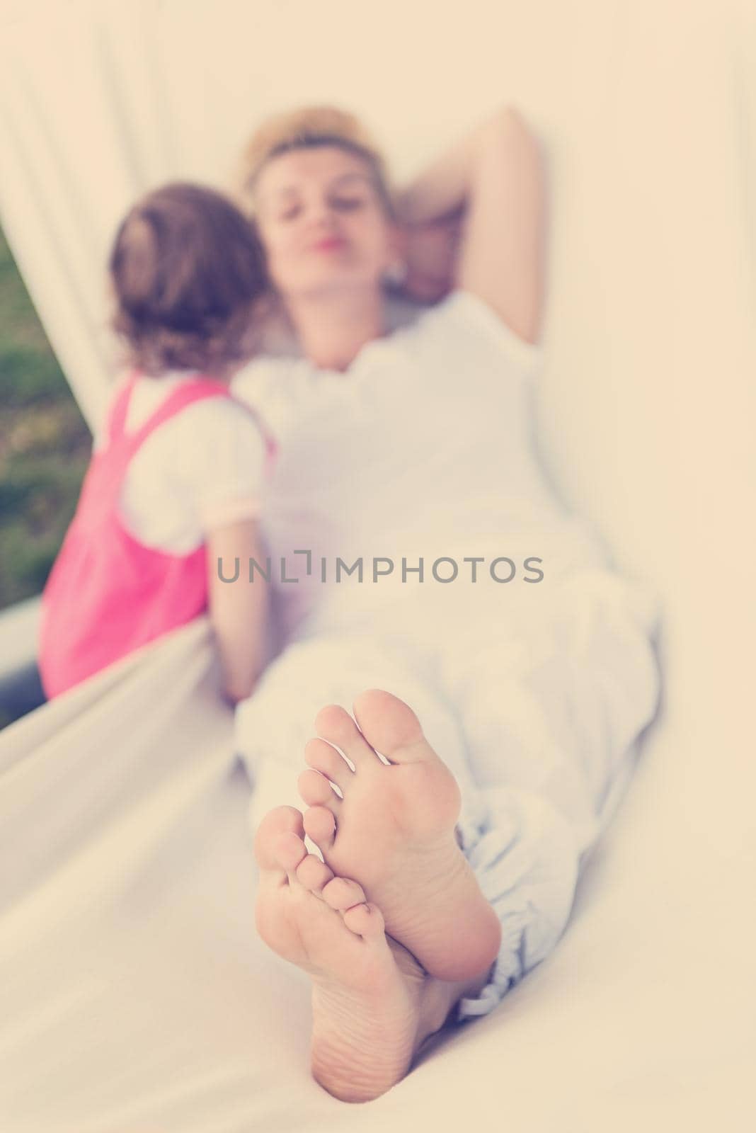 Happy mother and a little daughter enjoying free time hugging and relaxing in a hammock during a sunny day on holiday home garden