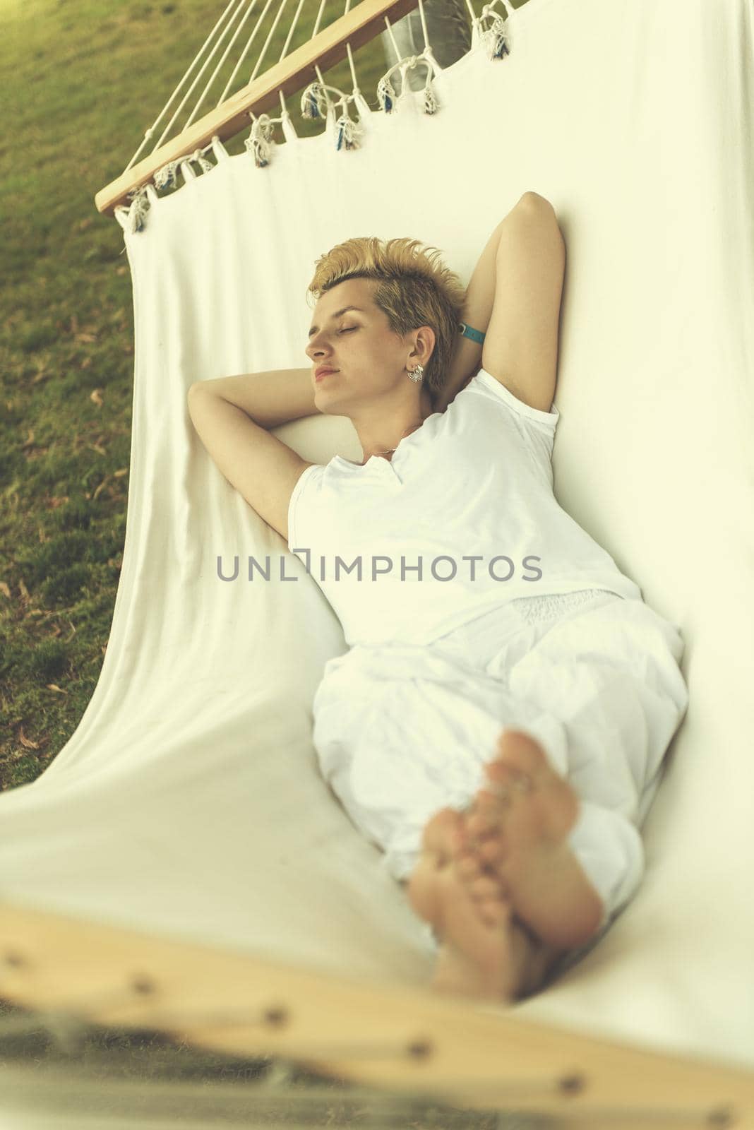 beautiful young woman enjoying free time while resting on white hammock in the backyard