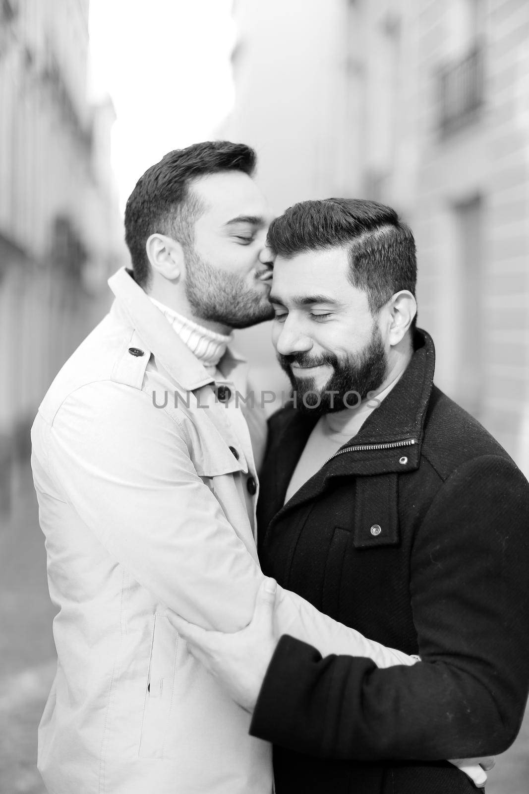 Black and white photo of two kissing gays in city, buildings i background. by sisterspro