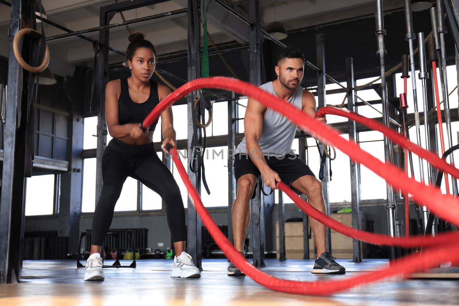 Athletic young couple with battle rope doing exercise in functional training fitness gym