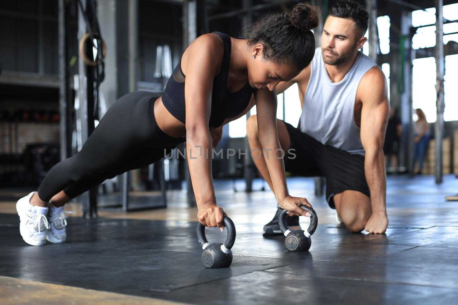 Sporty woman doing push-up in a gym, her boyfriend is watching her