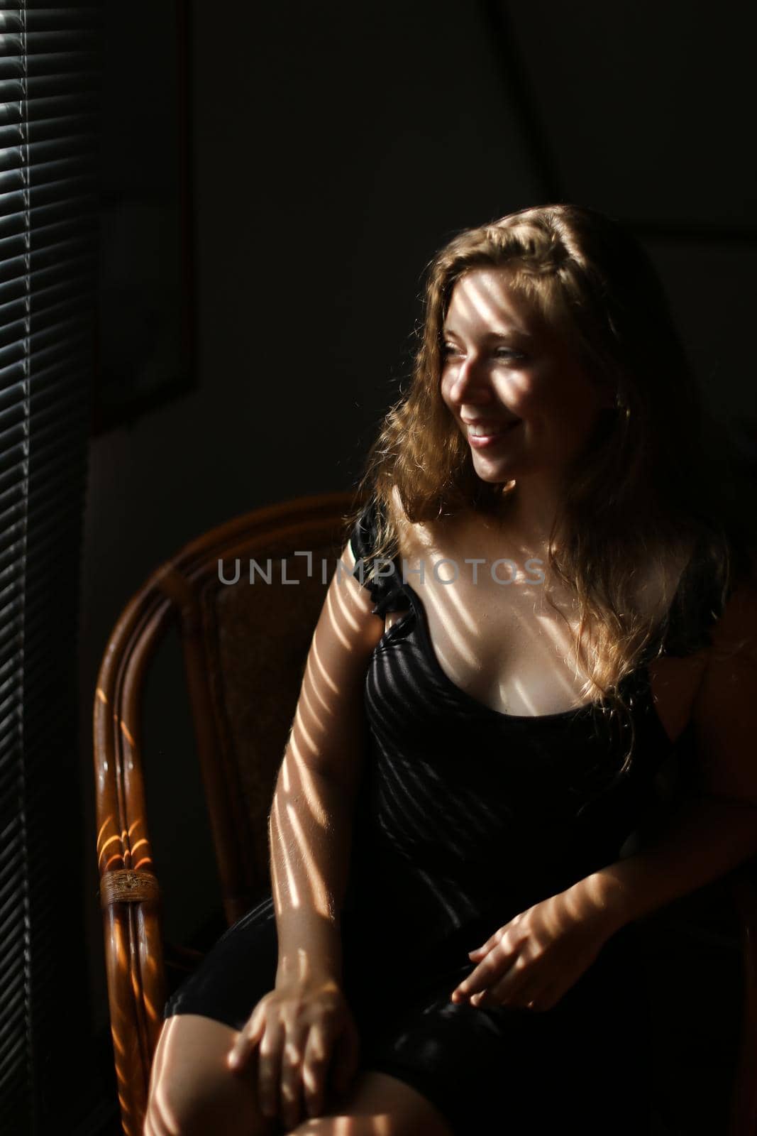 Portrait of young charming woman sitting in chair, striped shadows. Concept of female beauty and home photo session.