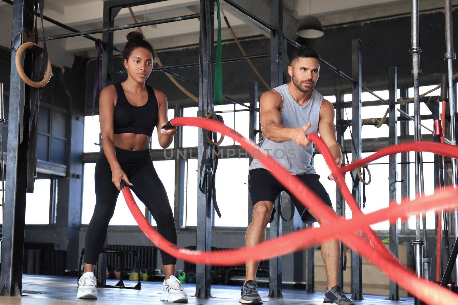 Athletic young couple with battle rope doing exercise in functional training fitness gym