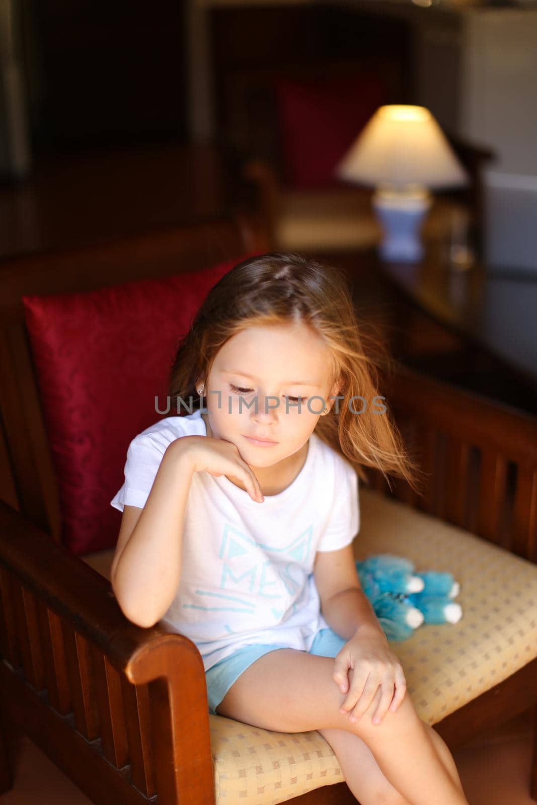 Little female caucasian kid sitting with toy in wooden chair. Concept of kid model and wood in interior.