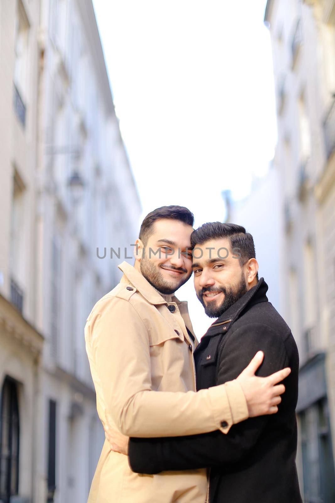 Two handsome caucasian hugging gays in city, buildings i background. Concept of same sex couple nad love.