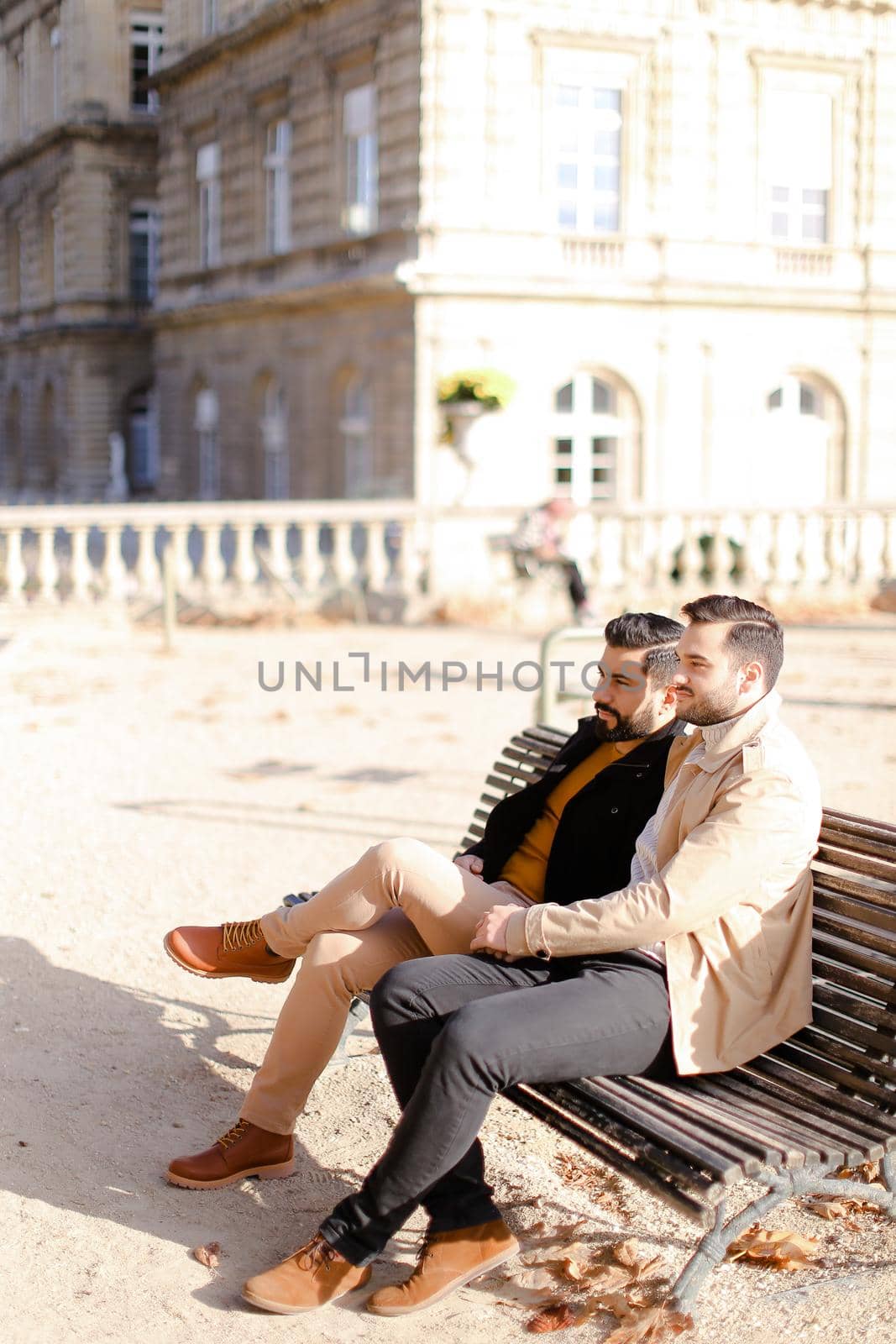 Two caucasian men sitting on bench near building. Concept of male friendship.