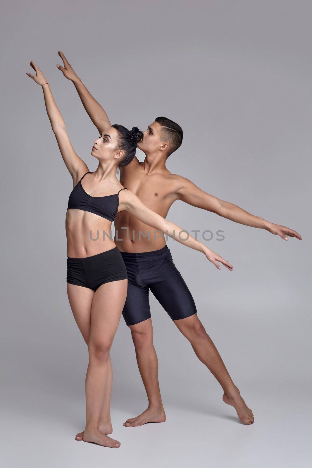 The couple of a young modern ballet dancers in black suits are posing over a gray studio background. by nazarovsergey