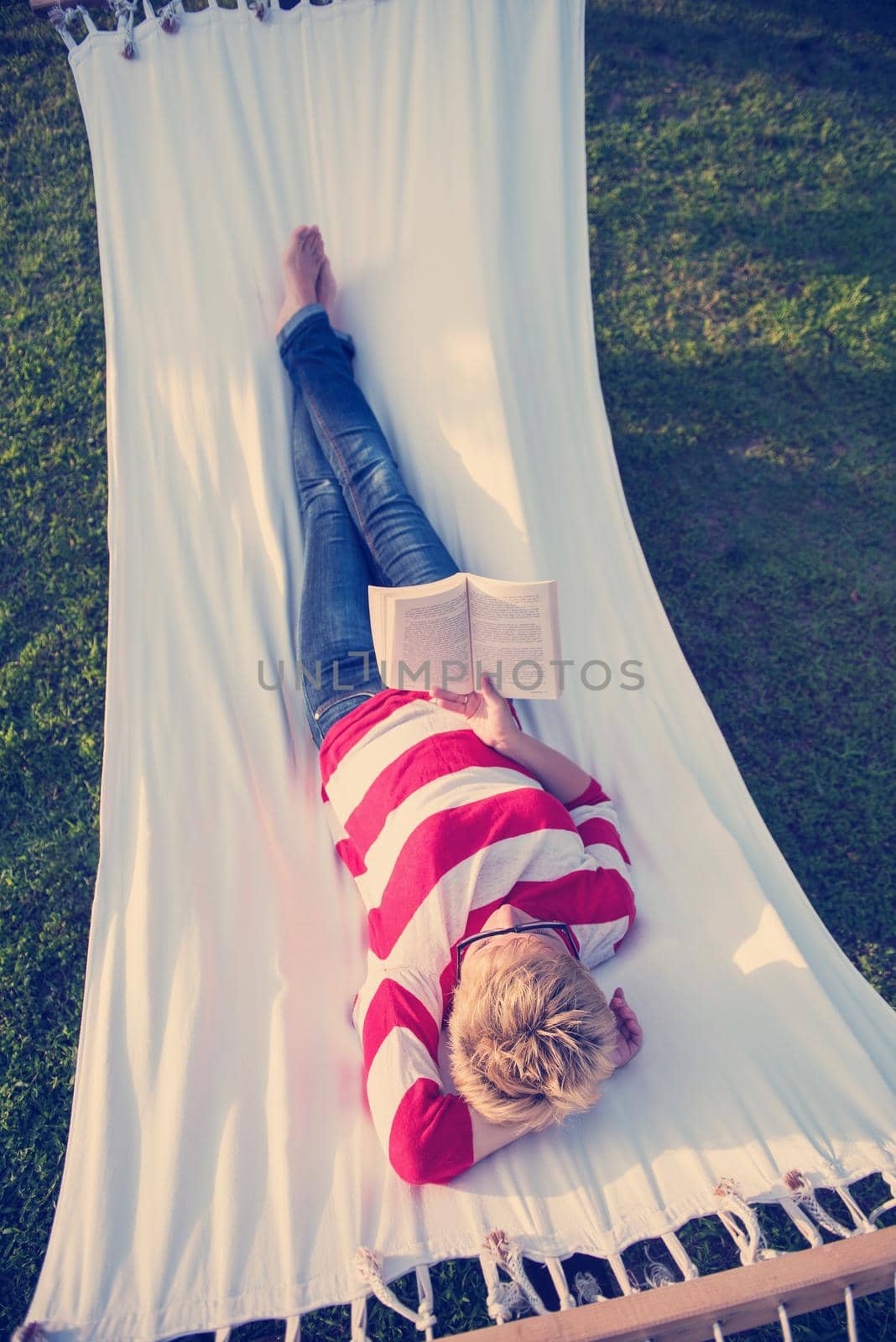 woman reading a book while relaxing on hammock by dotshock