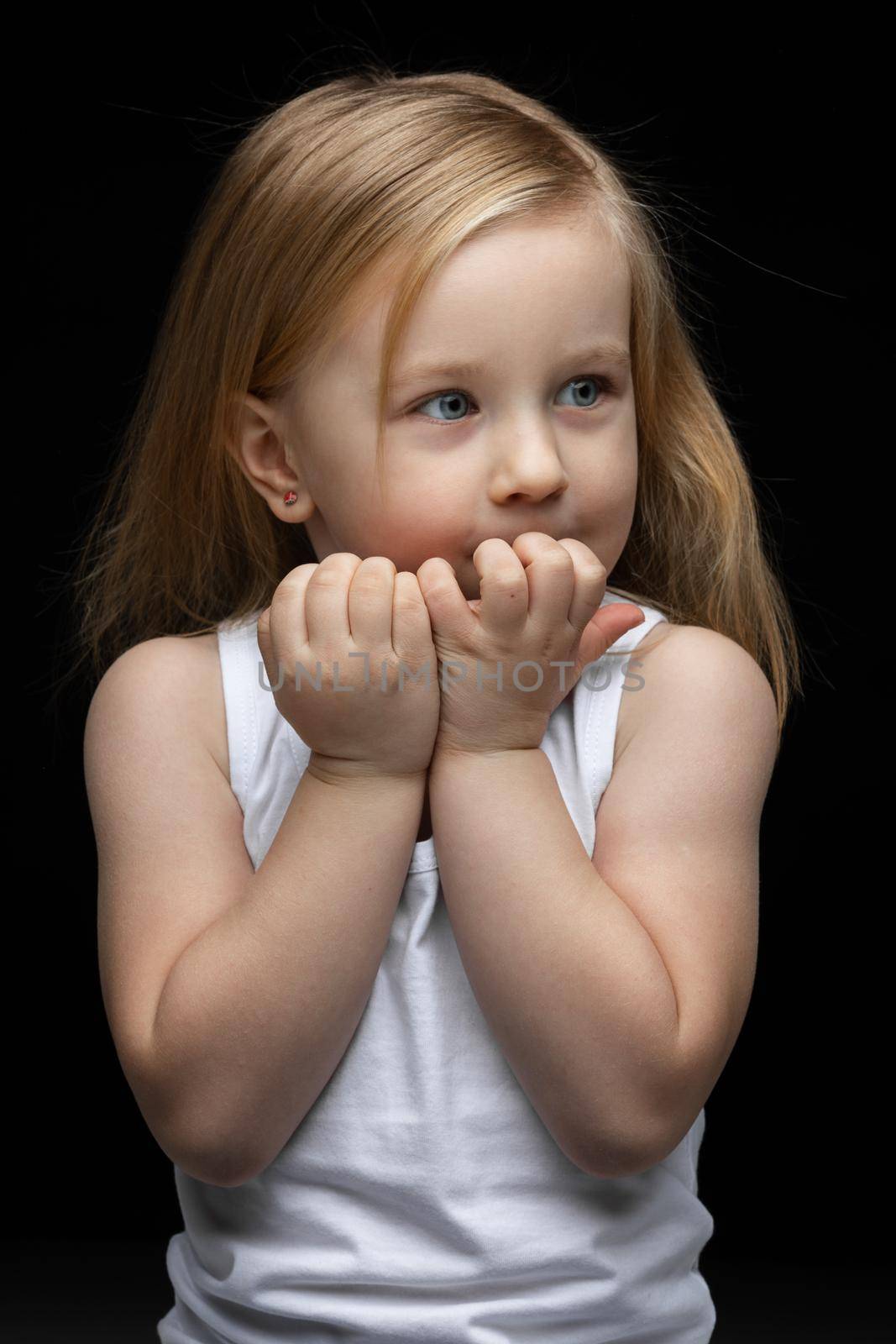 Cute little girl in a white undershirt putting hands to her face and looking away. Childhood concept