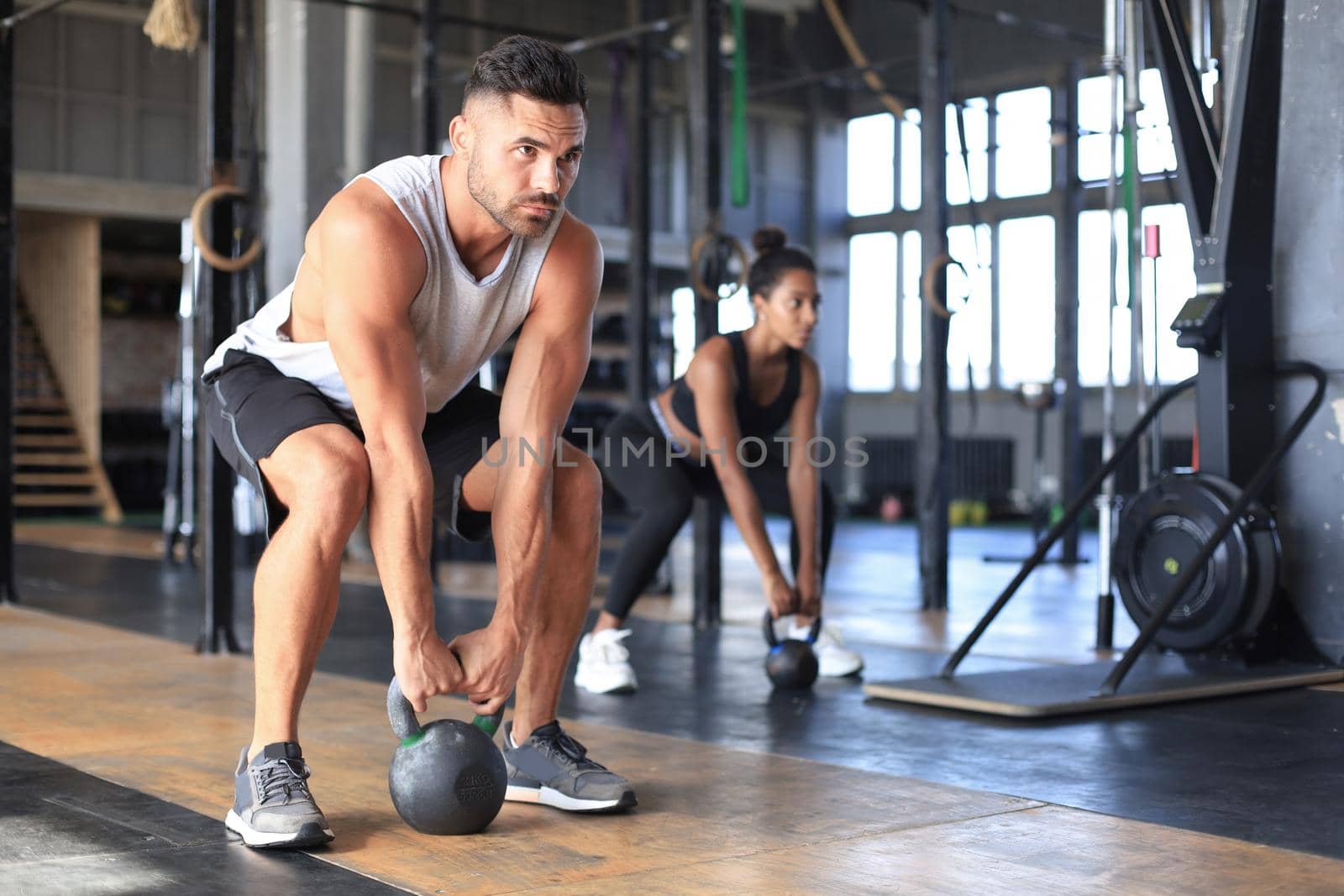 Fit and muscular couple focused on lifting a dumbbell during an exercise class in a gym