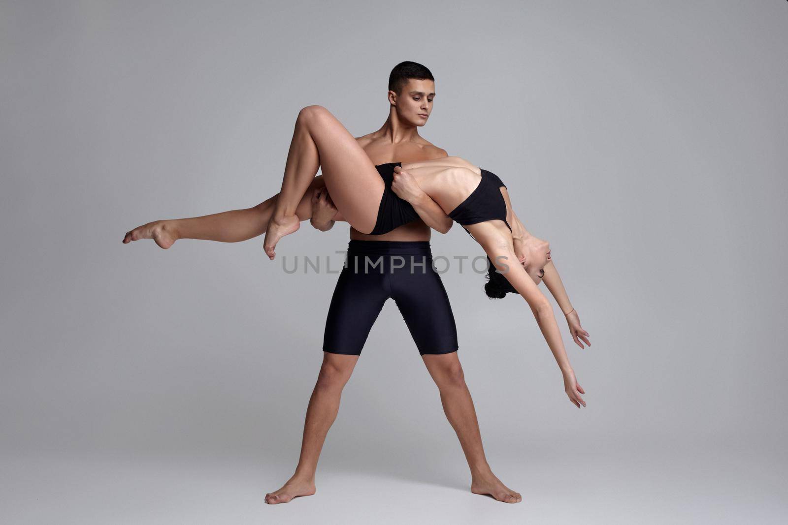 The couple of a young modern ballet dancers in black suits are posing over a gray studio background. by nazarovsergey