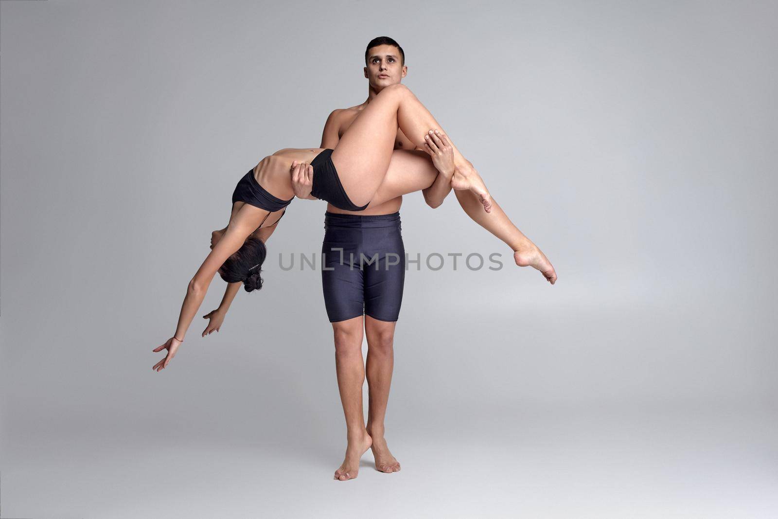 The couple of a young modern ballet dancers in black suits are posing over a gray studio background. by nazarovsergey