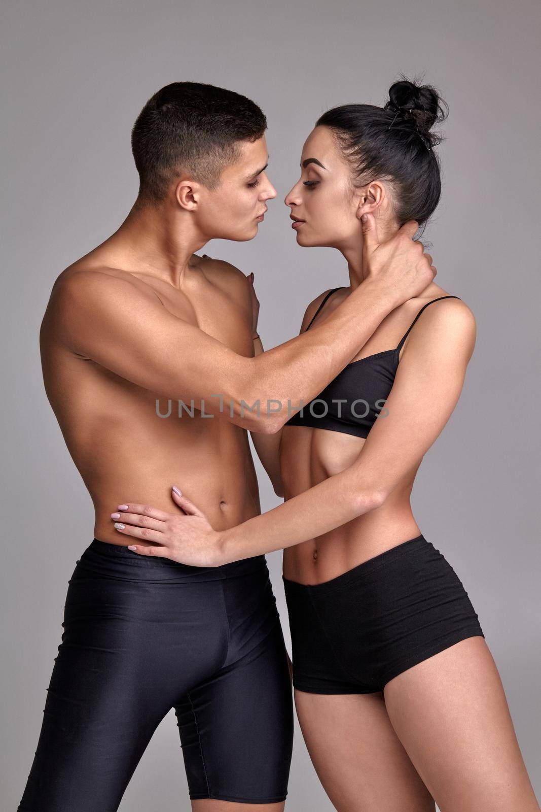 The couple of a young modern ballet dancers in black suits are posing over a gray studio background. by nazarovsergey