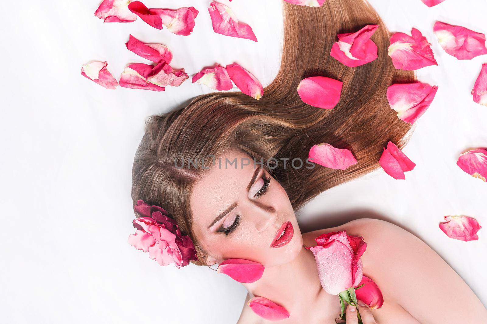 beautiful woman with rose lying among rose petals. photo with copy space
