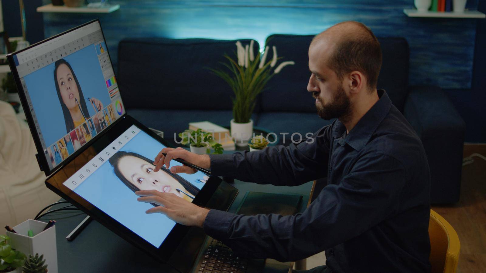 Media artist working on touch screen monitor to edit pictures in photography workspace. Man photographer using retouching software and graphic tablet with stylus on photos at studio.